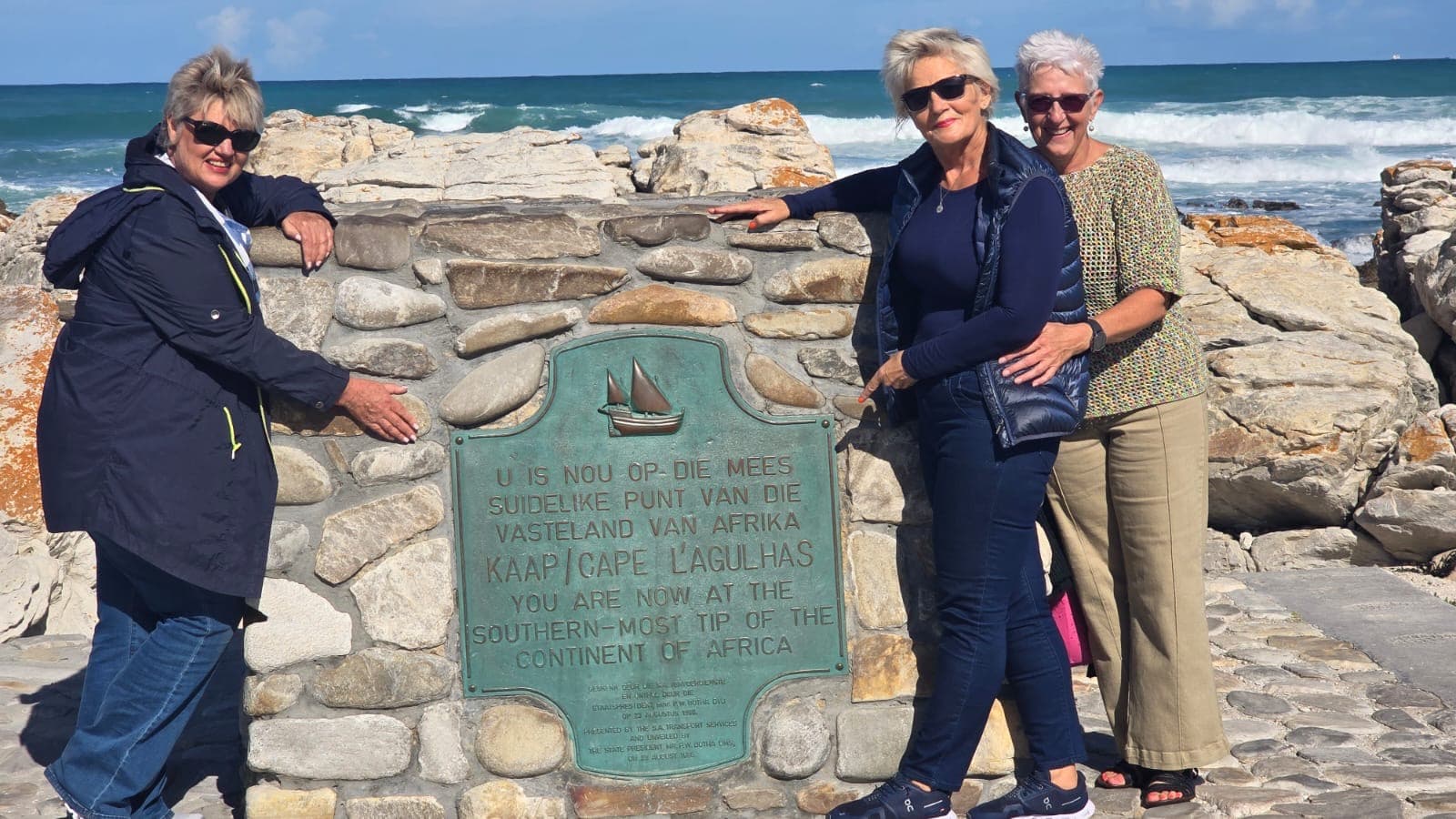 Three women posing by the stone monument at Cape Agulhas, the southernmost tip of Africa.